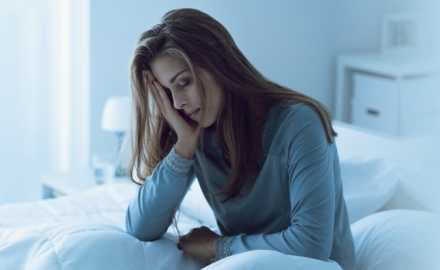 Women with head in hands sitting on a bed looking distressed 