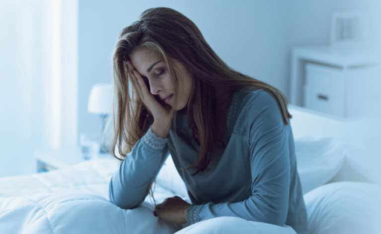 Women with head in hands sitting on a bed looking distressed 