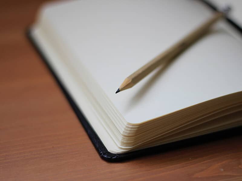 Black leather-bound notebook open to blank page with pencil resting on top.