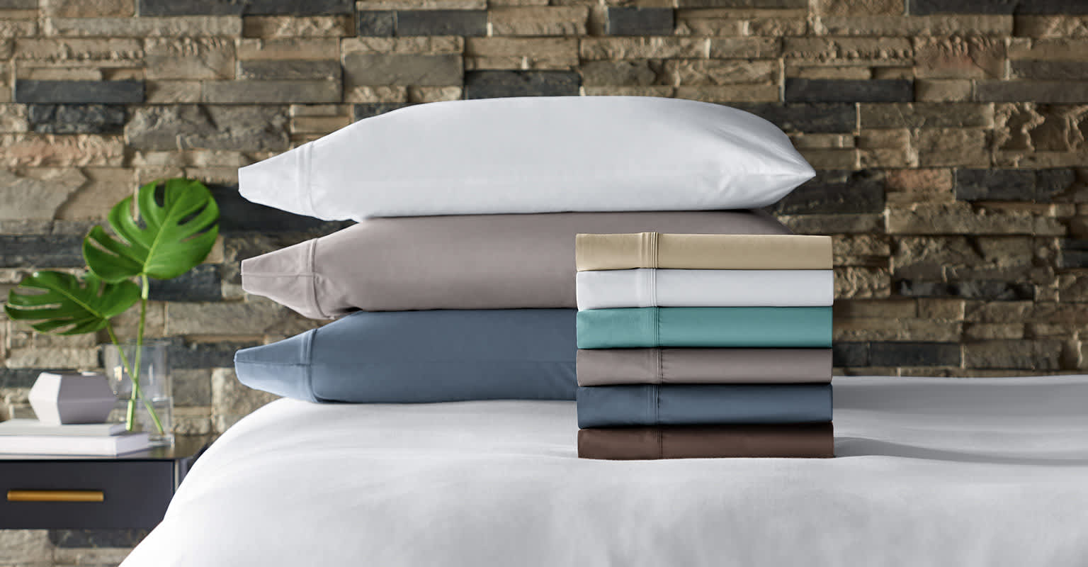 Stacks of crisp, soft-colored sheets and pillows next to sleek bedside table with modern accessories.