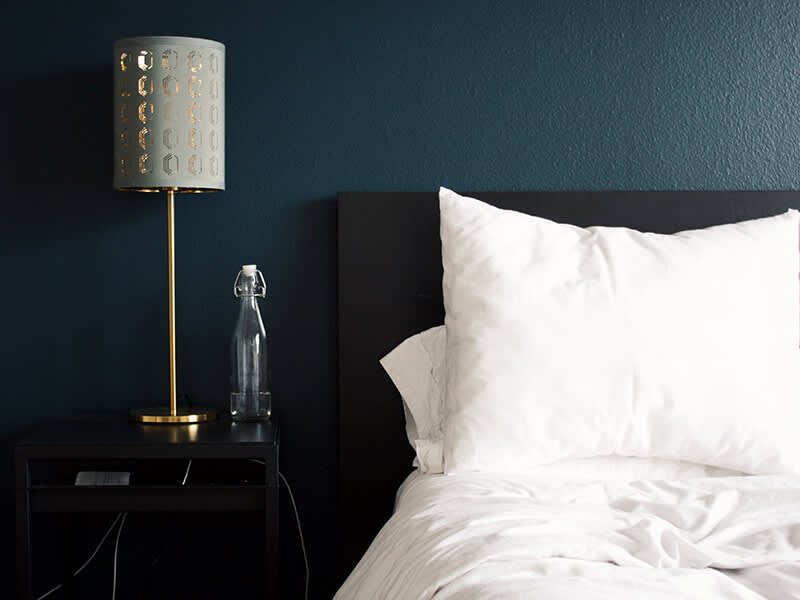 Rumpled white bedding in modern room setting. Sleek headboard, nightstand with gold lamp and bottle of water.