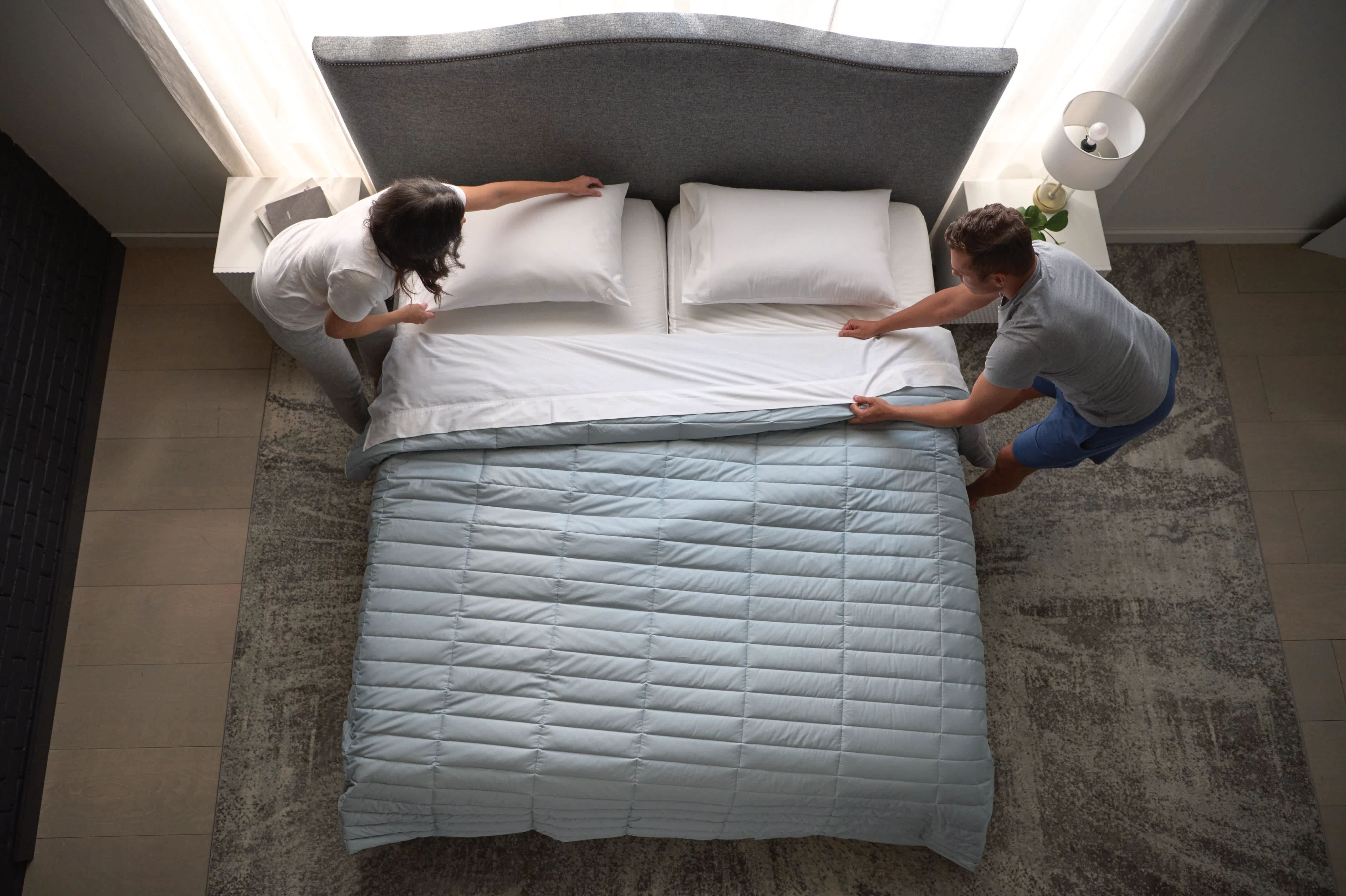 Two people making a Sleep Number bed with a light blue comforter