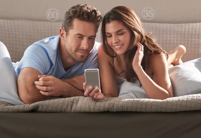 Couple sitting on bed looking at their phone showing Sleep Numbers