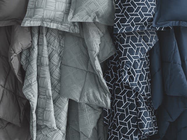 What is a comforter? Image of variety of different comforter colors. Text reads: It’s a bedding layer that goes on top of your bed, typically filled with down feather clusters of synthetic down alternative fibers to keep you warm. Comforters are designed with quilt patterns to keep the fill from shifting, so warmth is spread evenly throughout. Comforters are often available in colors and patterns to complement your bedroom décor. All Sleep Number® comforters have corner loops to keep them secure within our exclusive duvet covers. Link to shop now.