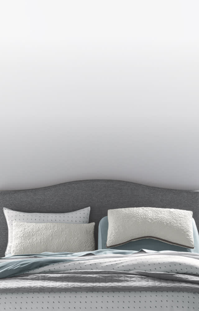 A variety of pillows in front of a grey upholstered headboard, how to choose a pillow that's right for you, link to shop all pillows